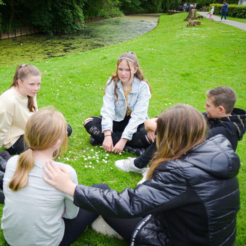 Bereaved military children sit in a circle on the grass. Scotty Members comfort each other. Military community